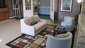 A lobby with a reception desk, a white sofa, a blue armchair, and a patterned rug. - Best Western Brentwood Inn (Brentwood)
