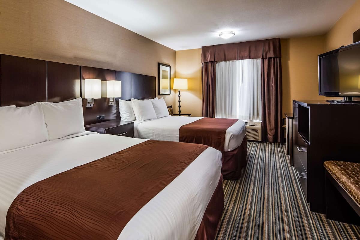 A hotel room with two beds, a TV, a desk, and a window with curtains.