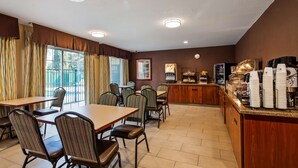 A dining area with tables and chairs, a buffet counter with coffee machines, and a view of the outdoors through large windows. - Best Western Brentwood Inn (Brentwood)