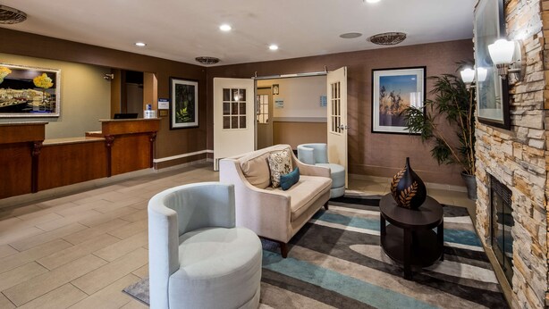 A lobby with a reception desk, a sofa, a chair, a decorative vase, and a stone wall. - Best Western Brentwood Inn (Brentwood)