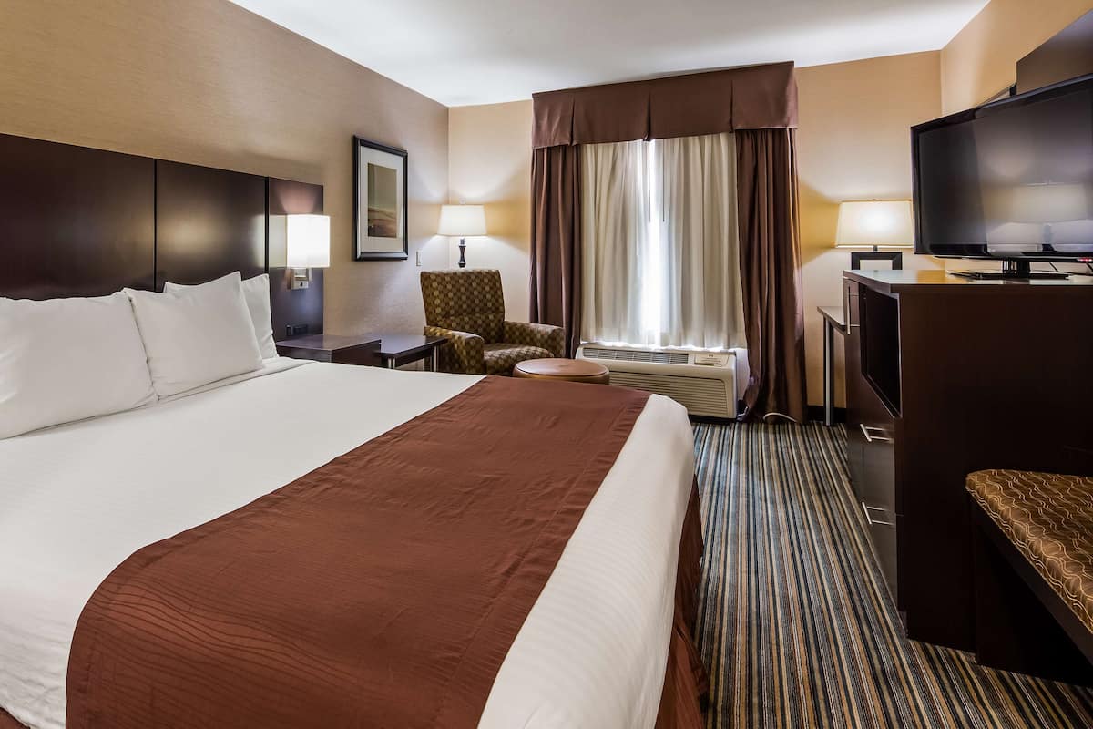 A hotel room with a large bed, a desk with a television, a chair, a lamp, and a window with curtains.