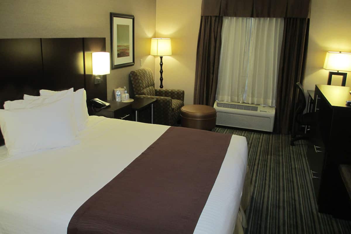 Ein Hotelzimmer mit einem großen Bett, einem Schreibtisch, einem Stuhl, einer Lampe und einer Klimaanlage.