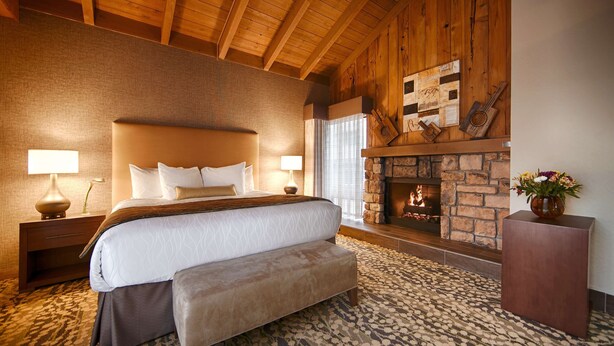 A bedroom with a large bed, wooden ceiling beams, a stone fireplace, and a patterned carpet. - Best Western The Inn & Suites Pacific Grove (Pacific Grove)