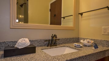 A bathroom with a granite countertop, a sink, a mirror, a towel dispenser, and a soap dish.