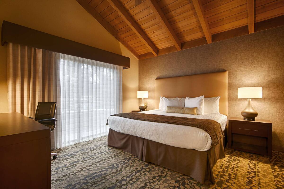 A hotel room with a large bed, two bedside tables with lamps, a desk, and a chair.