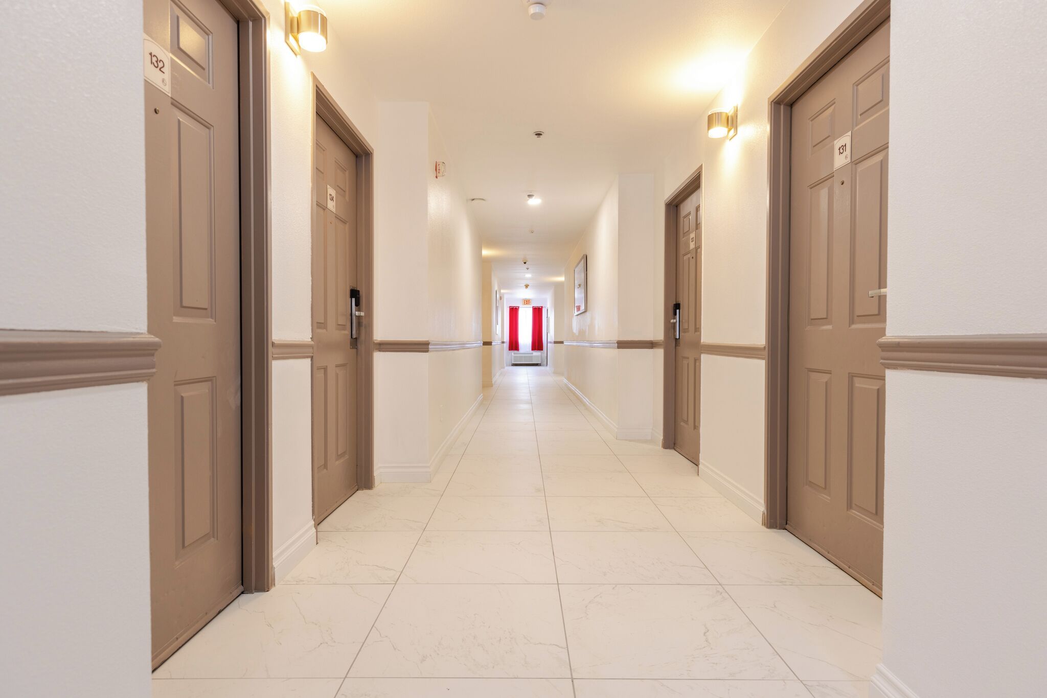 A hotel hallway with doors numbered 132 and 133, leading to a red curtain at the end.