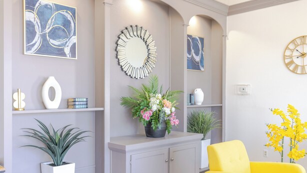 A living room with a grey sofa, yellow armchair, and a white cabinet with decorative items and plants.