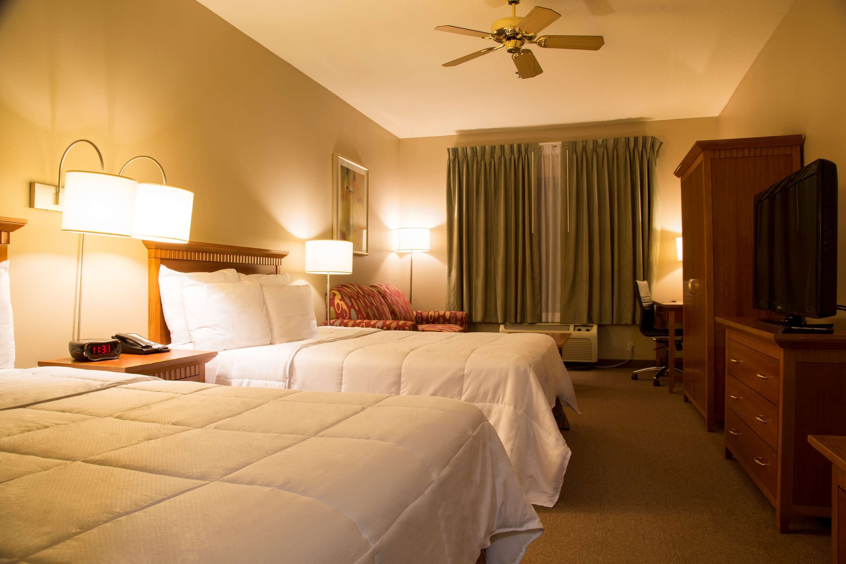 A hotel room with two beds, a ceiling fan, a TV, and a desk with a lamp.
