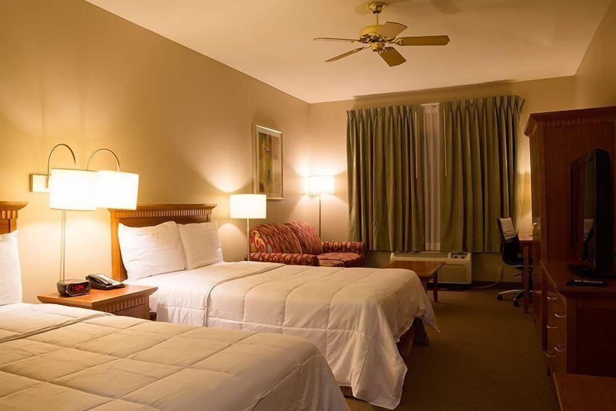 A hotel room with two beds, a ceiling fan, a desk with a chair, a television, and a window with curtains.