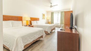 A hotel room with two beds, a desk, a television, and a ceiling fan.