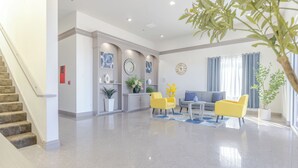 A spacious living area with a staircase, a sofa, yellow chairs, and a dining area with a clock and decorative items.