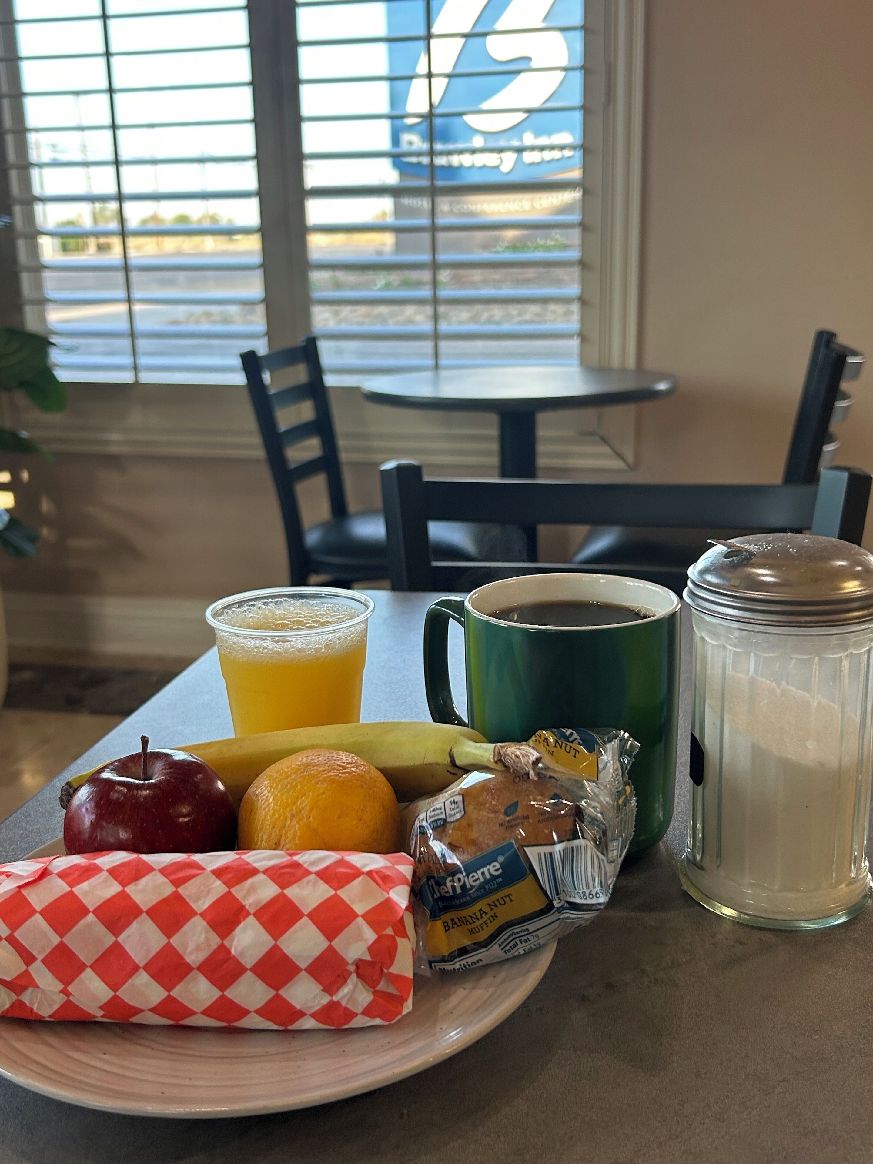 A breakfast tray with a muffin, juice, coffee, an apple, an orange, and a banana.