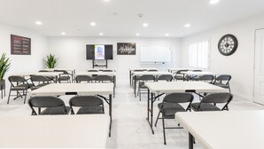 A conference room with white tables and chairs, a clock, and motivational posters on the walls.