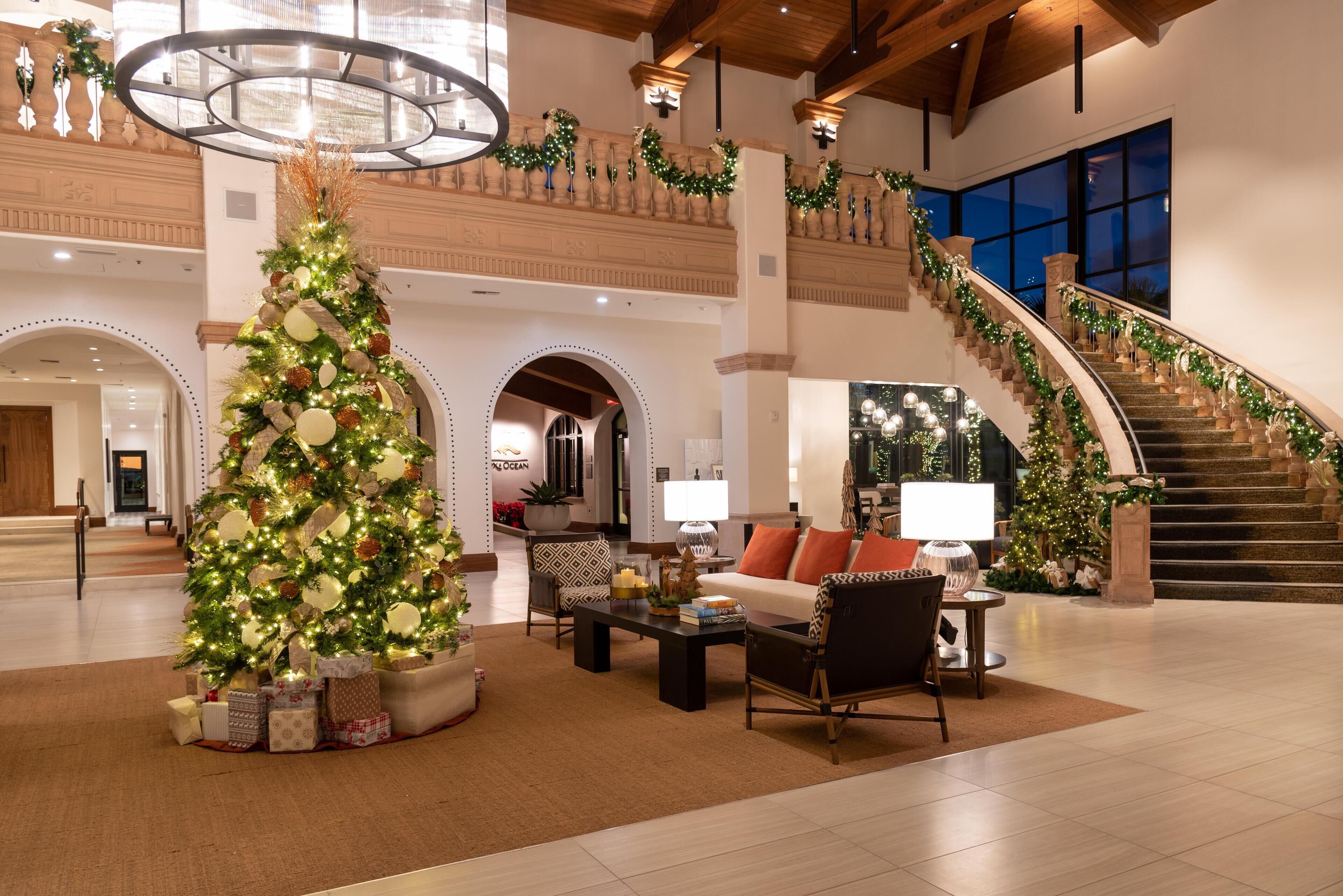 A spacious lobby with a large Christmas tree, comfortable seating, a staircase, and a view of the ocean.