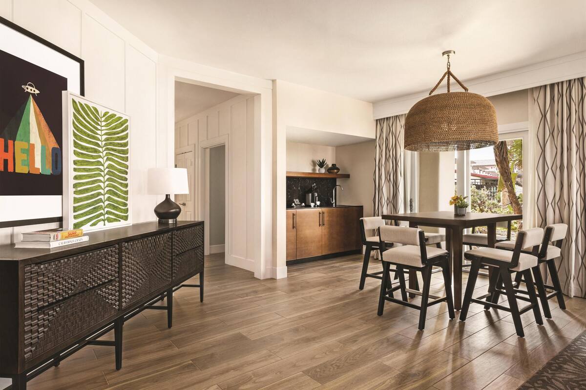 A modern kitchen with wooden cabinets, a dining area with a round table and chairs, and a hanging light fixture.