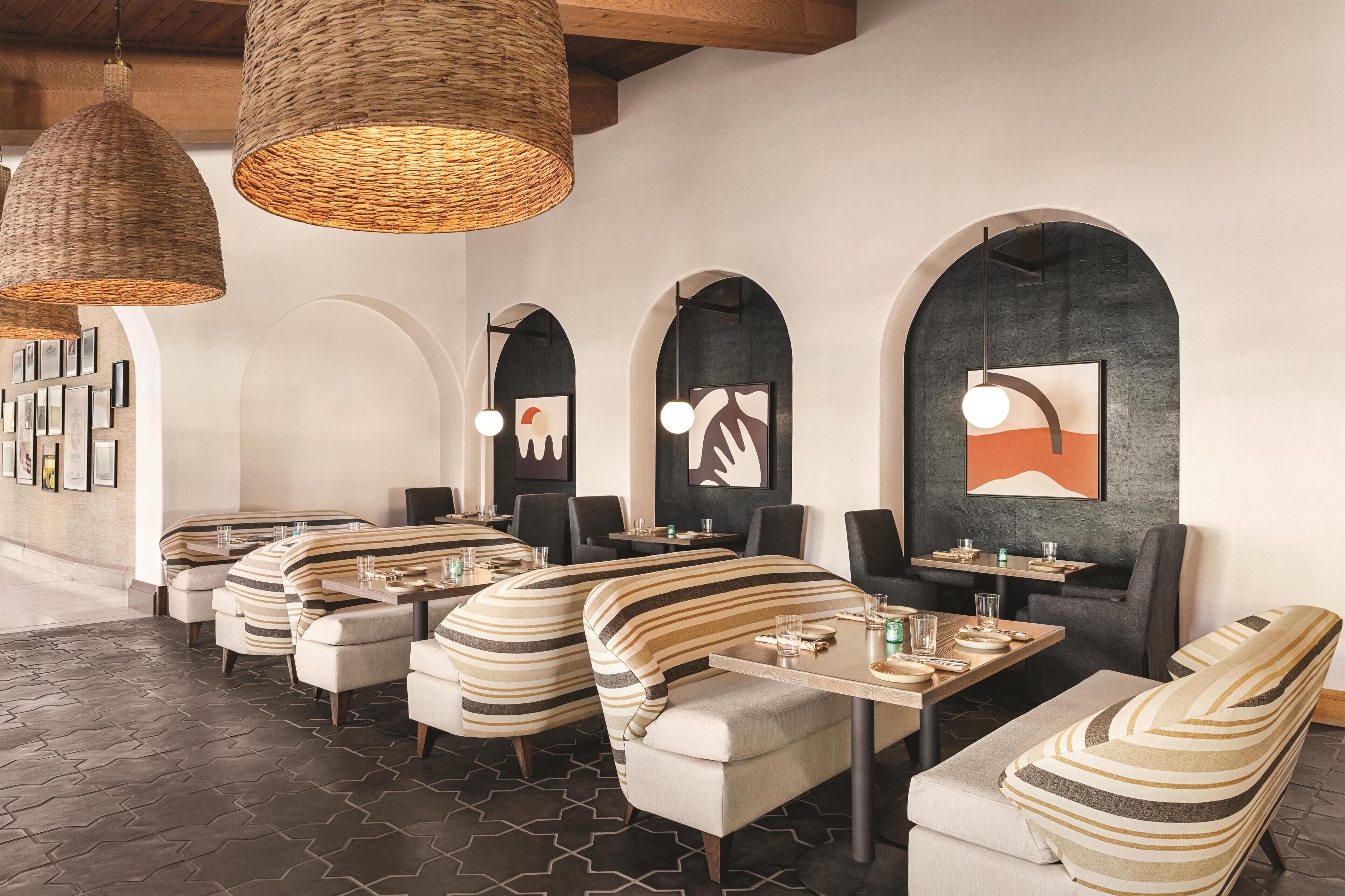A modern restaurant with striped cushioned seating, dark patterned flooring, and large woven pendant lights.