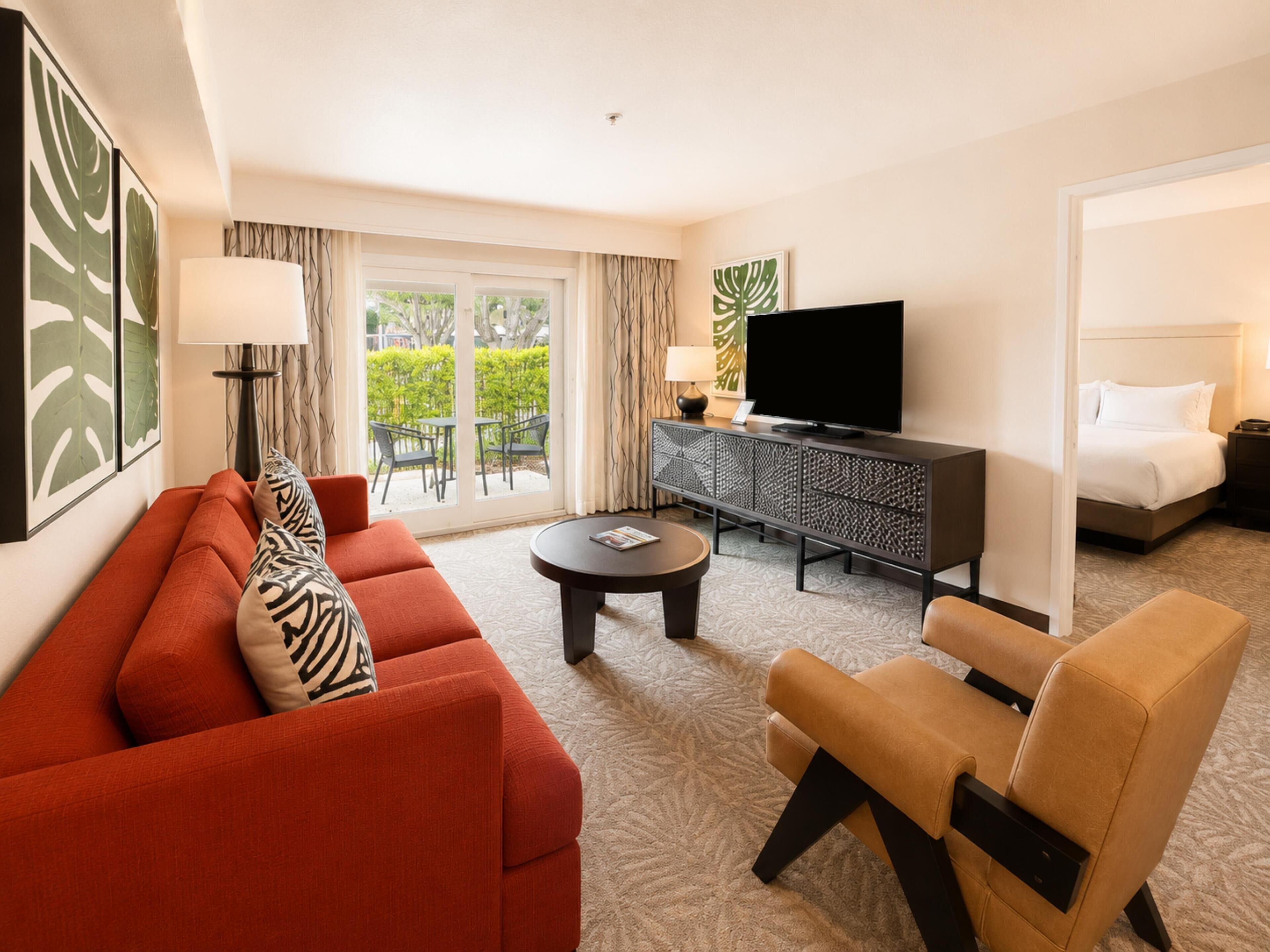 Habitación de hotel con sofá, sillón, televisor y vistas a zonas verdes.