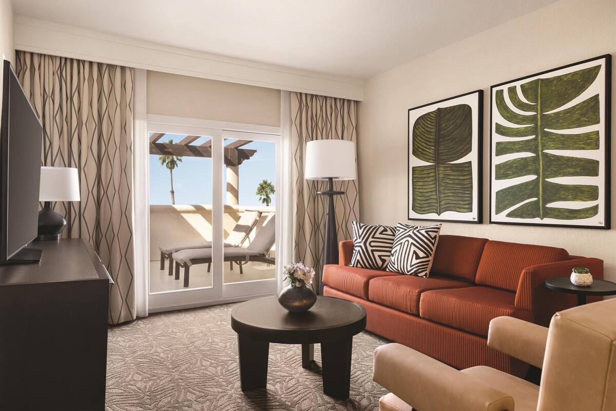 A hotel room with a sofa, a coffee table, a TV, and a view of the outdoors.