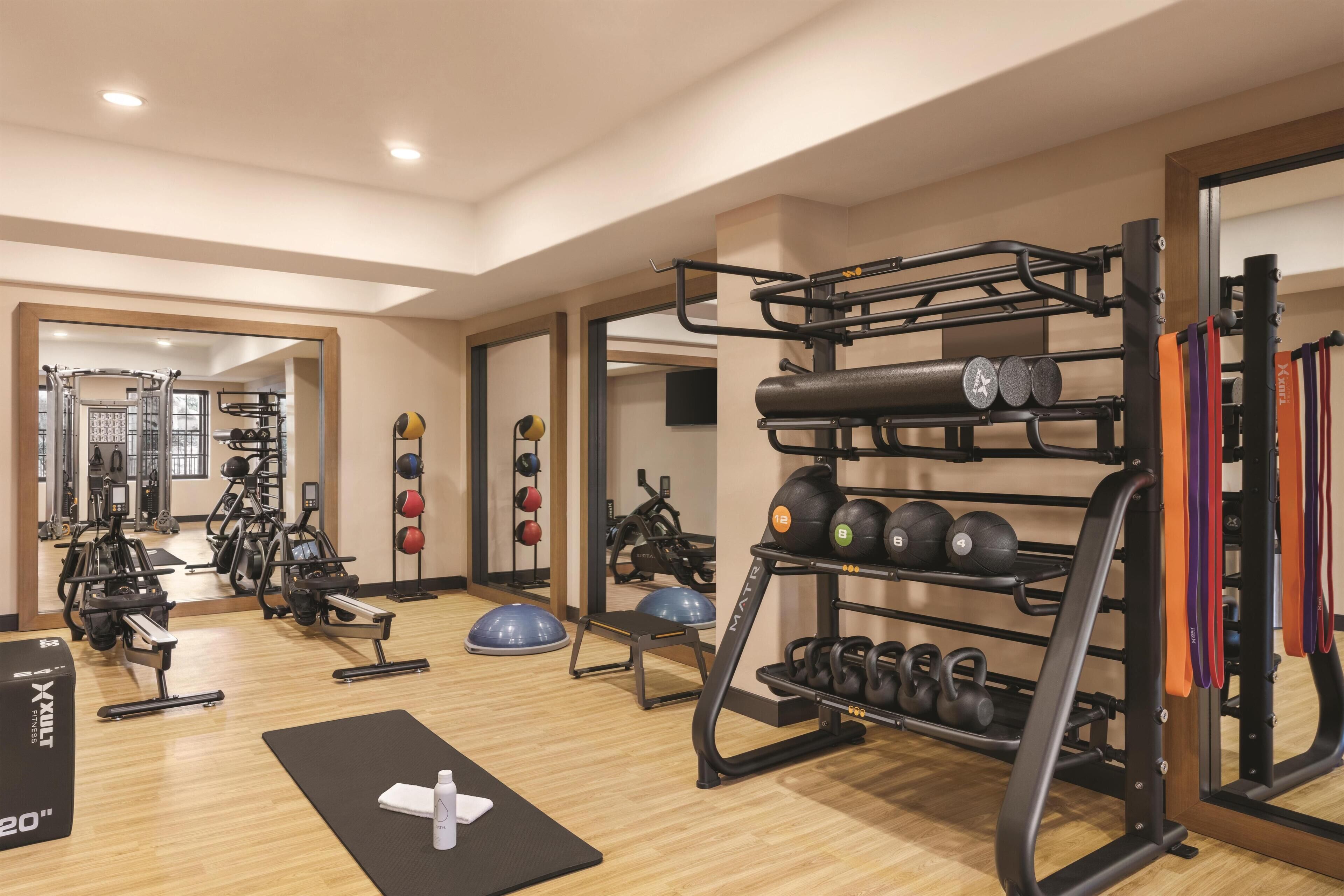 A gym with exercise equipment, a mirror, and a wooden floor.