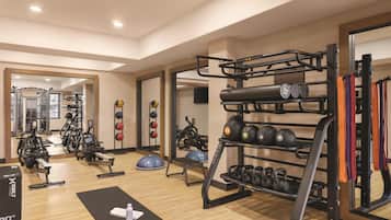 A gym with exercise equipment, a mirror, and a wooden floor.