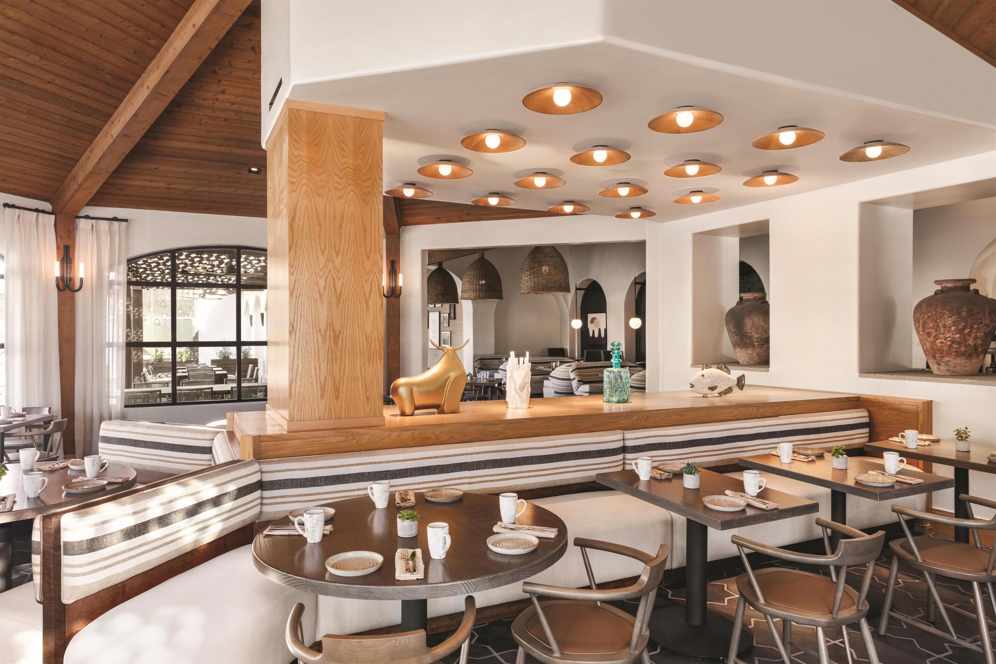 A modern restaurant with round tables, wooden accents, and a central seating area with a decorative animal statue.