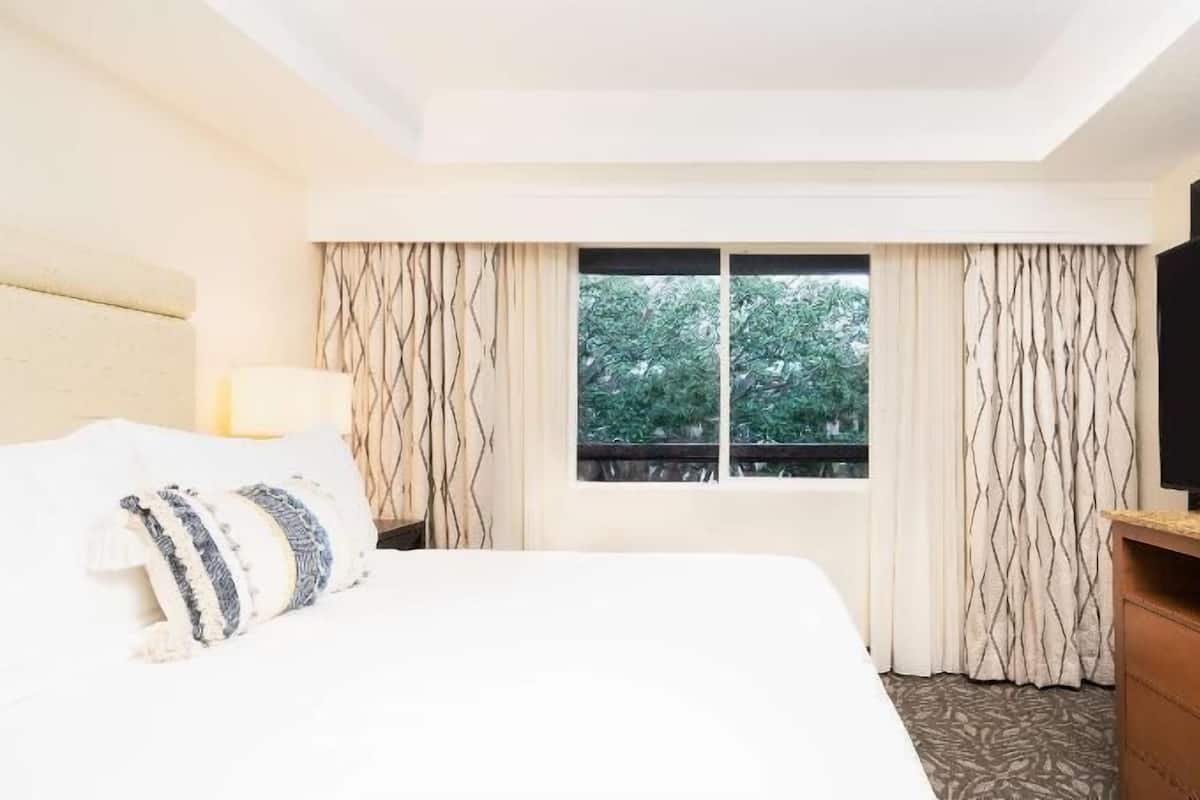 A hotel room with a bed, a TV, a window with curtains, and a dresser.