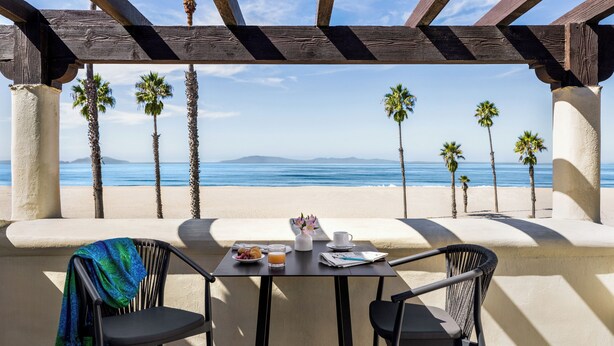 Un tavolo con vista sulla spiaggia e sull'oceano, una sedia con una coperta e un tavolino con una tazza e un piatto di cibo.