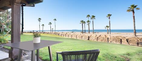 A patio with a table and chair overlooking a beach with palm trees and a clear sky.