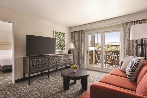 Una habitación de hotel con sofá, televisor, mesa de centro y balcón con mobiliario exterior.