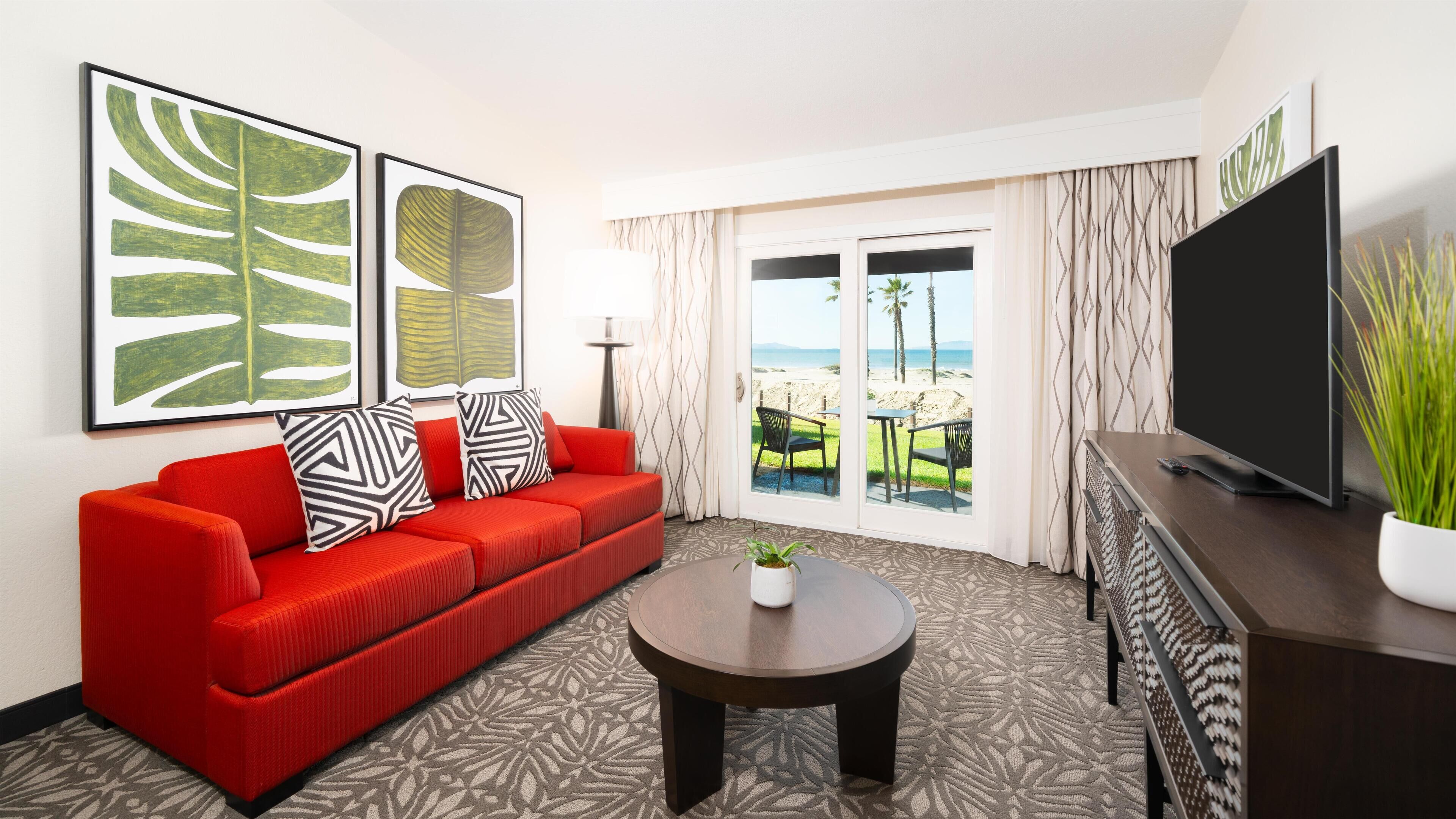 Une chambre d’hôtel avec un canapé rouge, un téléviseur à écran plat, une table basse et une vue sur la plage.