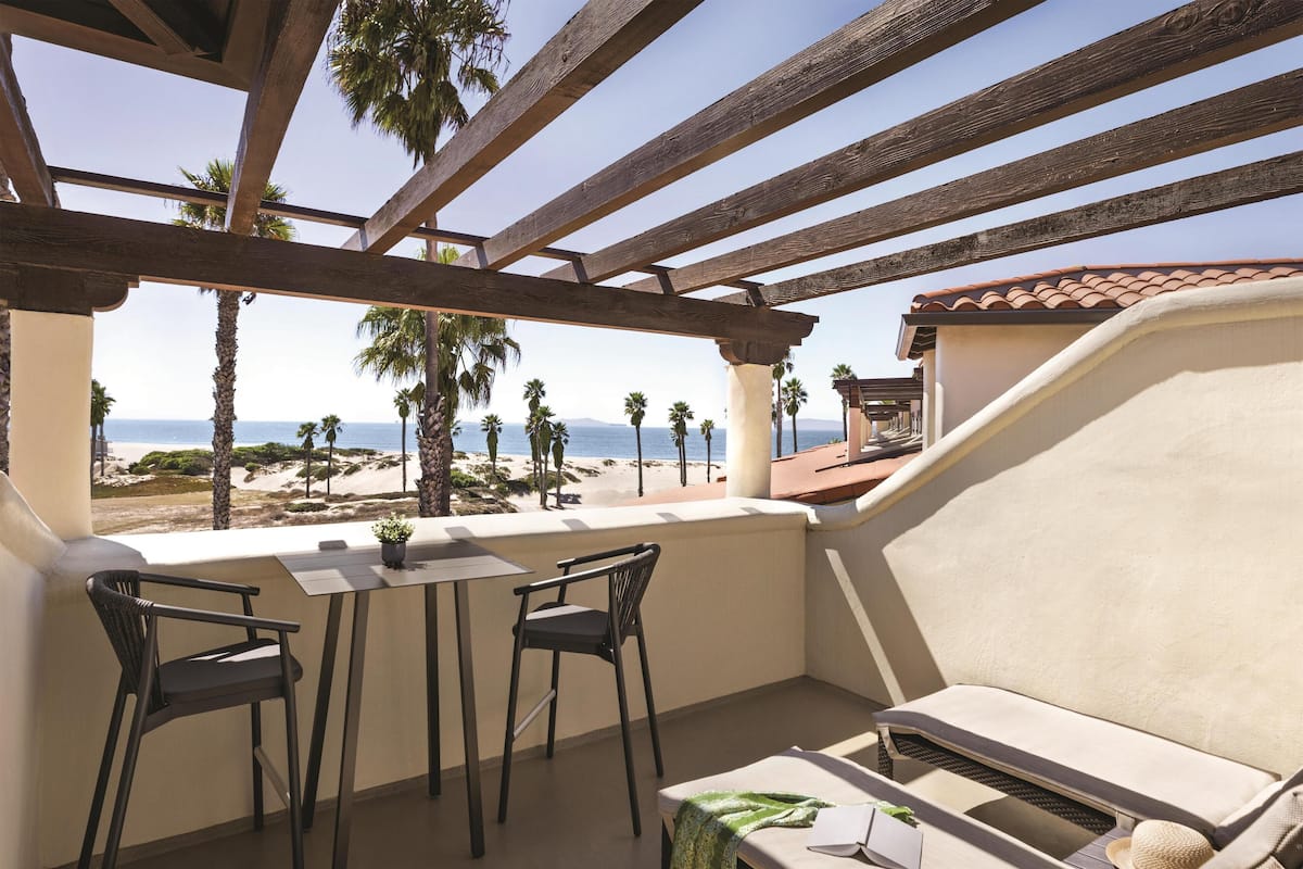 A balcony with a wooden pergola, two chairs, a table, and a sofa.