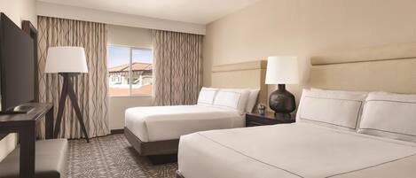A hotel room with two beds, a desk, a chair, a lamp, and a ceiling fan.
