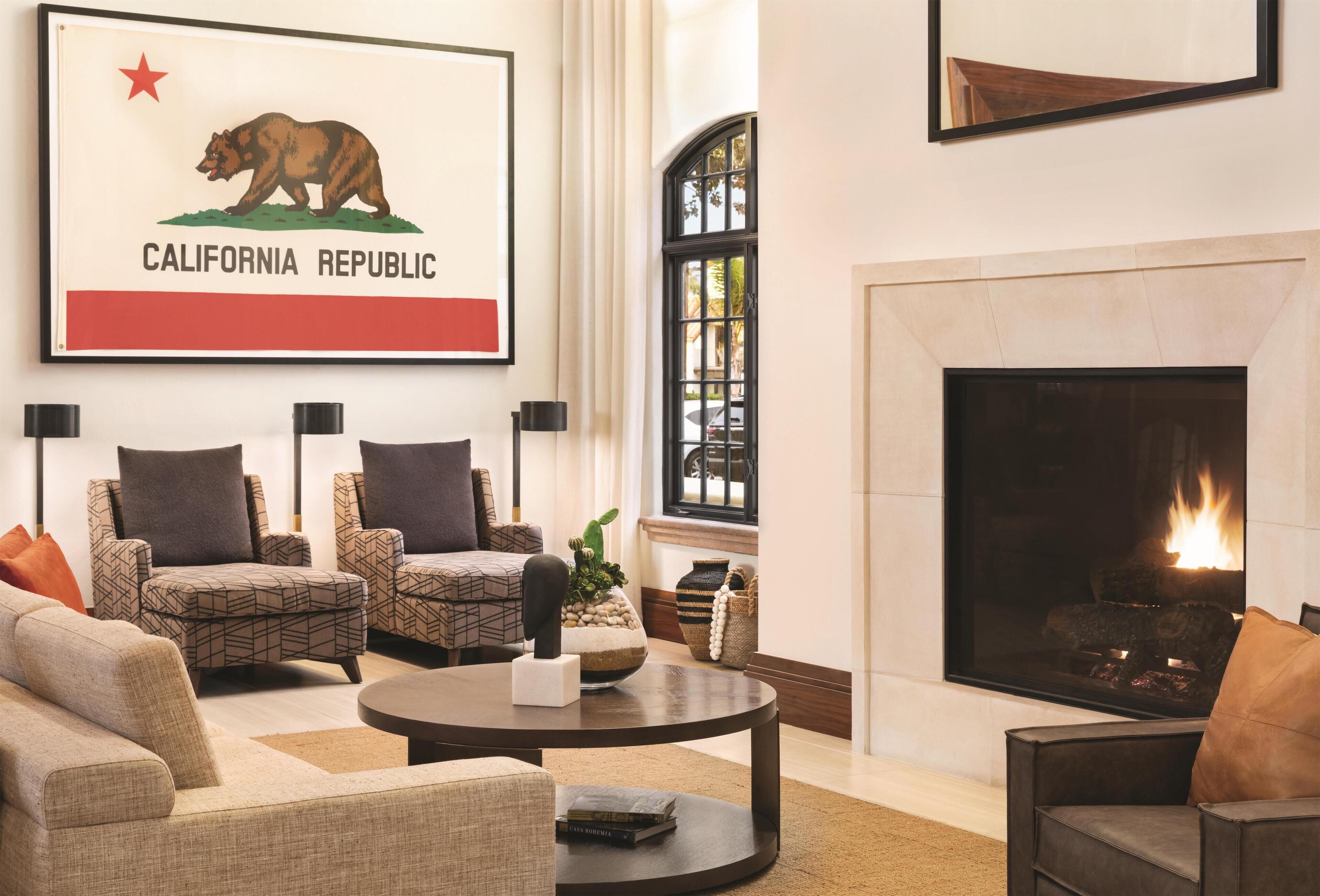 A living room with a fireplace, two armchairs, a sofa, and a coffee table. A framed California Republic flag is on the wall.