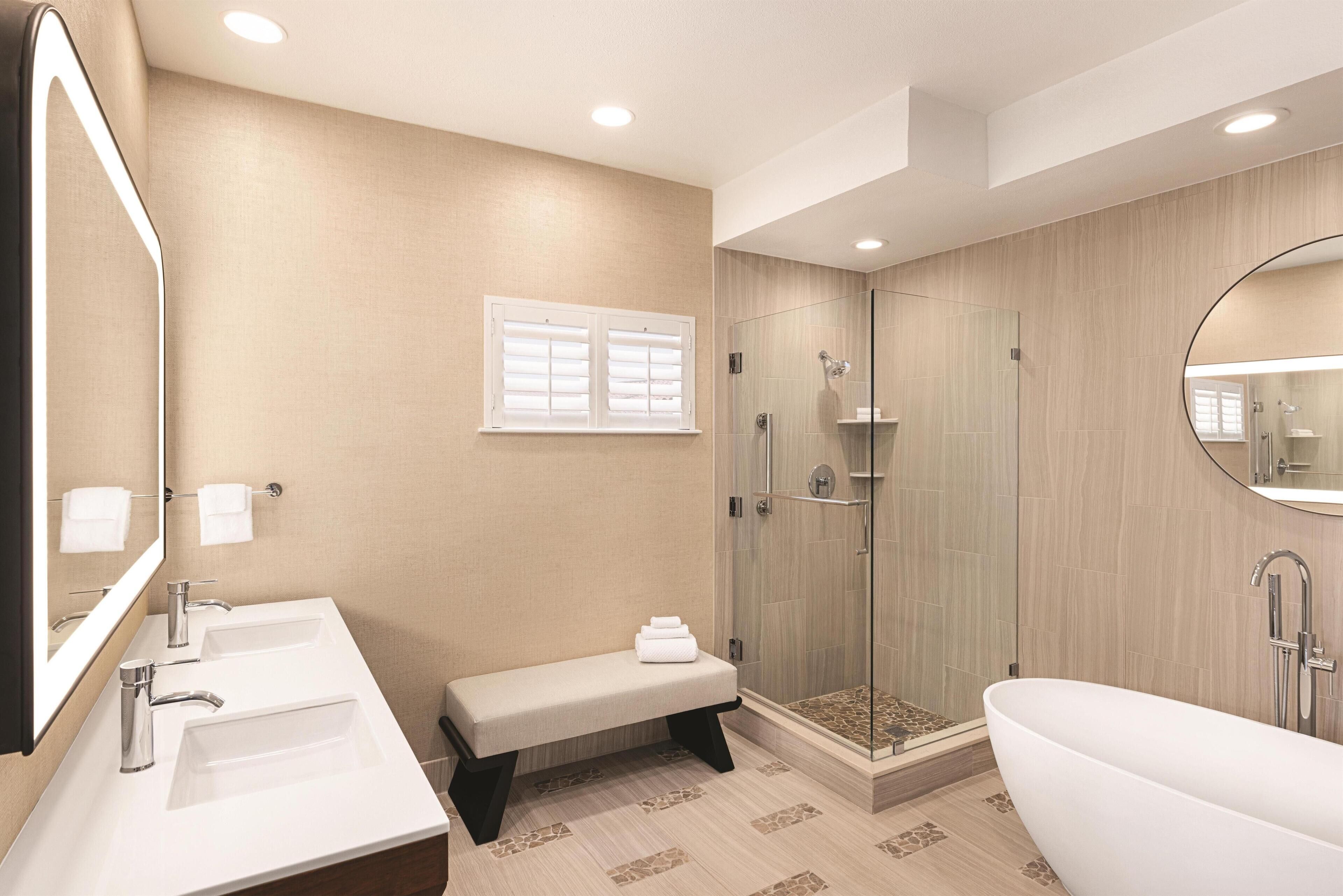 Un baño moderno con dos lavamanos, un banco, ducha a ras de suelo y bañera independiente.