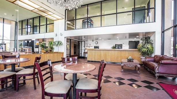 Eine geräumige Lobby mit Schachbrettmuster-Boden, mehreren Sitzbereichen einschließlich runder Tische und Stühle, einem Empfangstresen und einem großen Fenster mit Blick ins Innere.