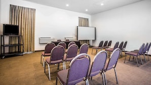 Ein Konferenzraum mit Reihen violetter Stühle, einer Projektionsleinwand und einem Fernseher auf einem Podest.