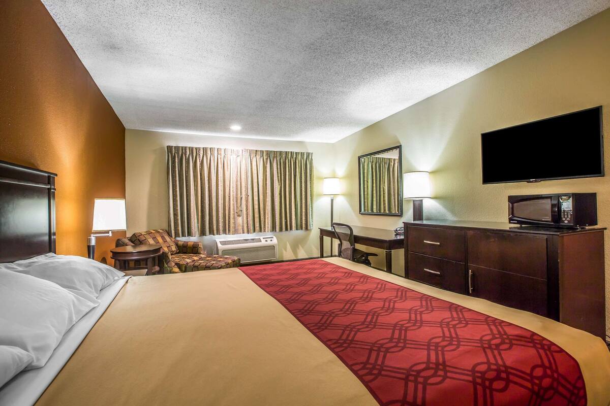 Ein Hotelzimmer mit Bett, Schreibtisch, Fernseher und Spiegel.
