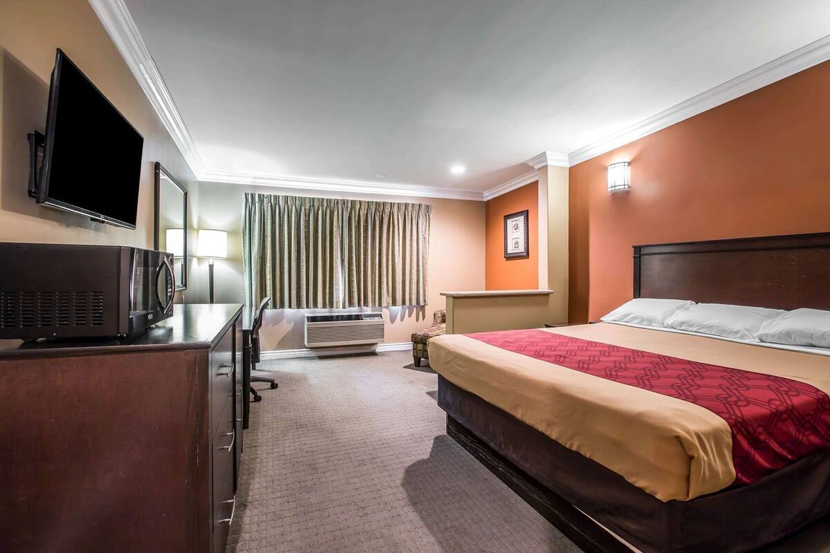Ein Hotelzimmer mit Bett, Schreibtisch, Flachbildfernseher, Klimaanlage und einem Fenster mit Vorhängen.