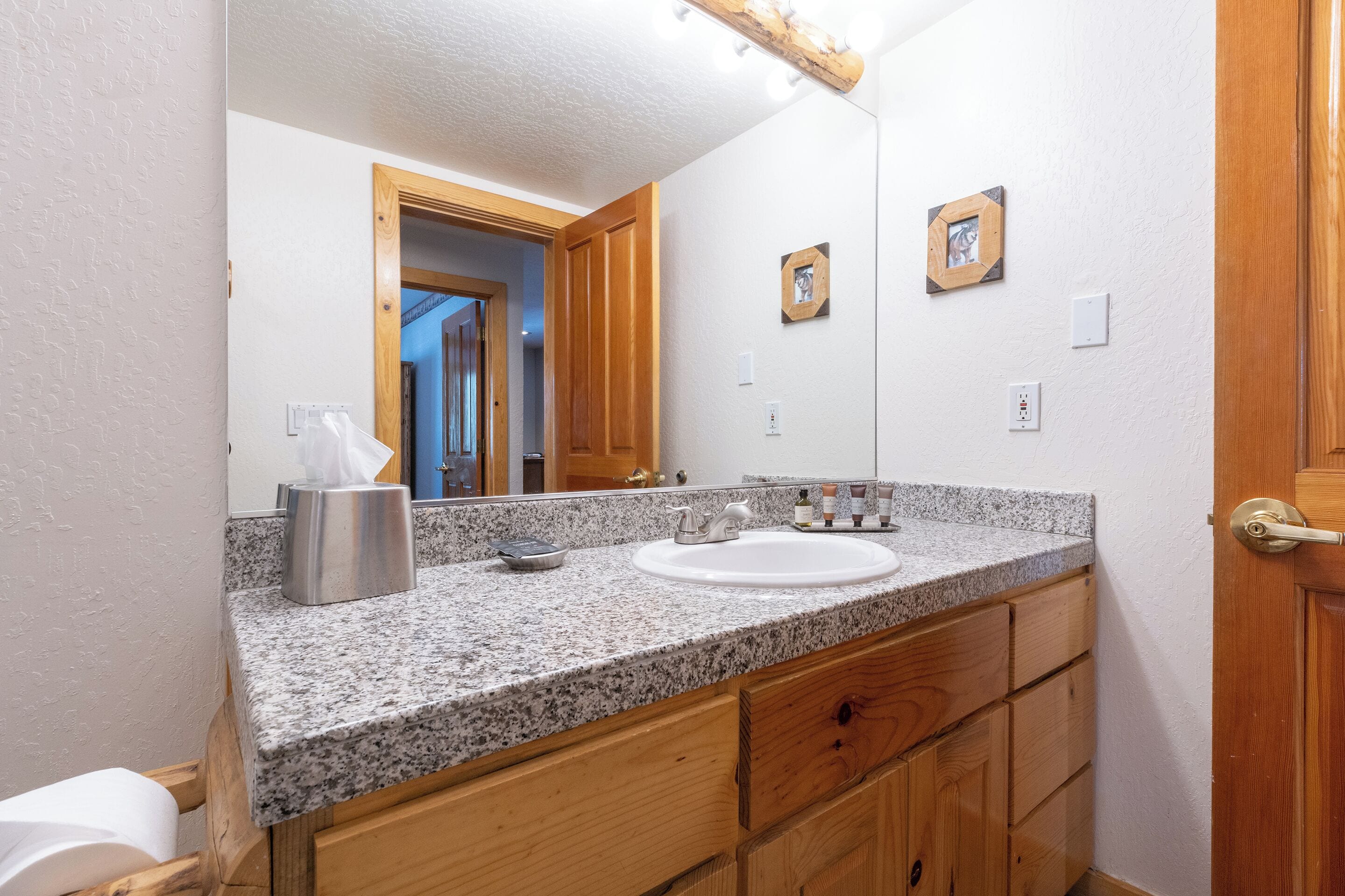 Un baño con encimera de granito, armarios de madera, lavabo blanco y espejo.