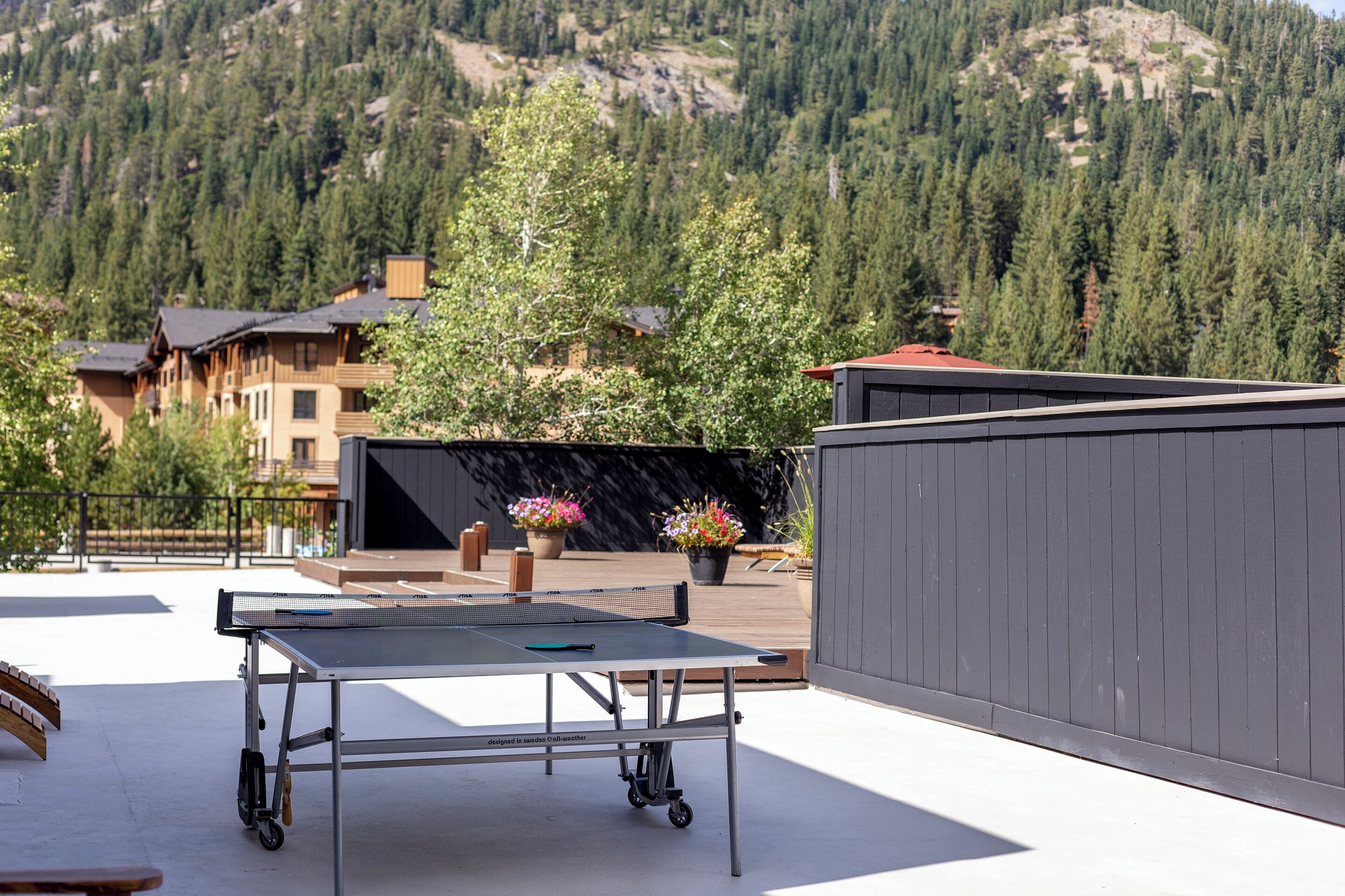 A ping pong table on a rooftop with a mountain view, potted plants, and a wooden deck.