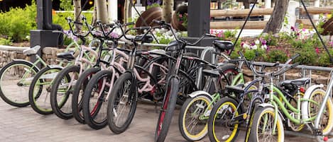 A row of bicycles parked in an outdoor area with a stone wall and greenery.