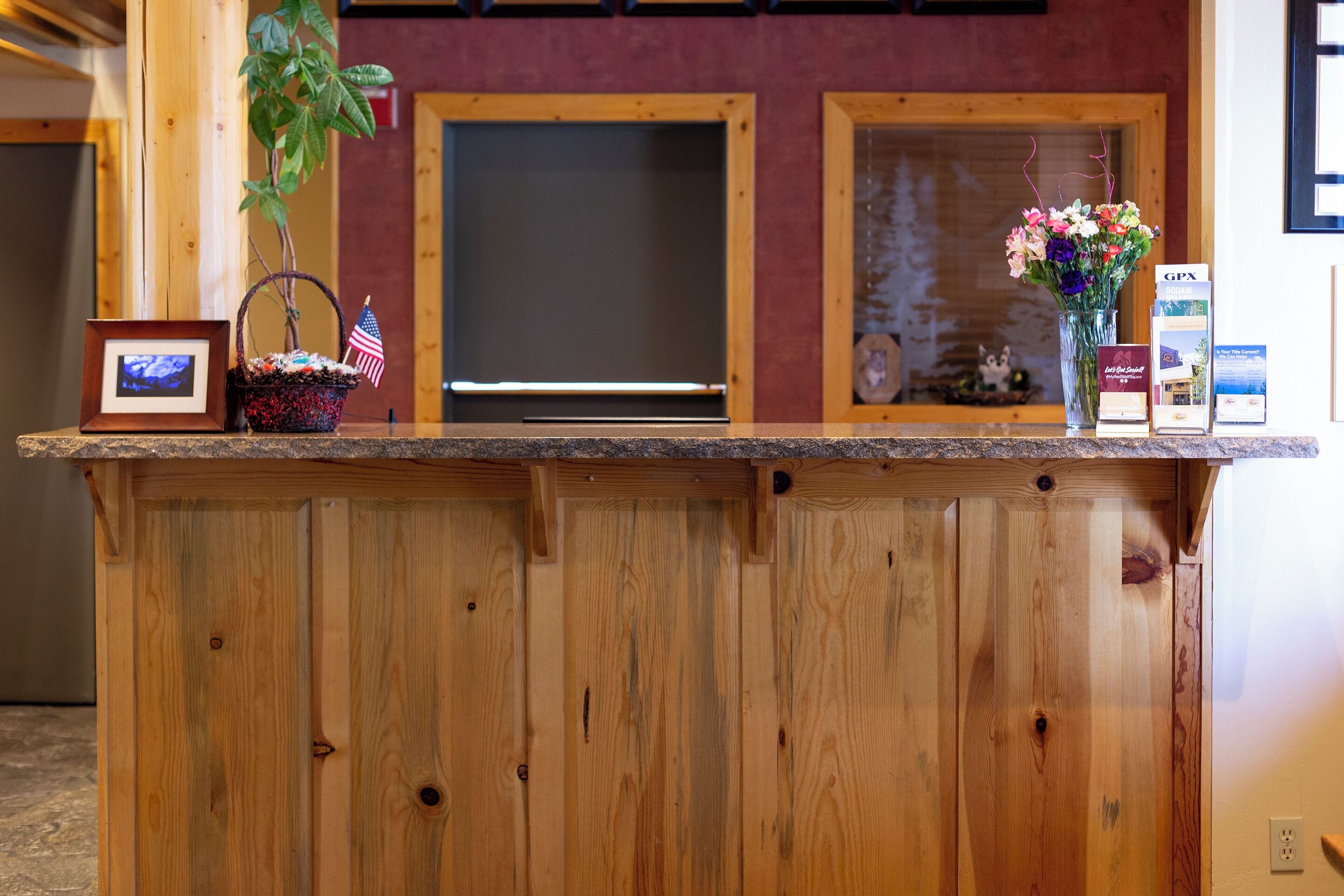 A wooden reception desk with a framed picture, a small American flag, and a vase of flowers.