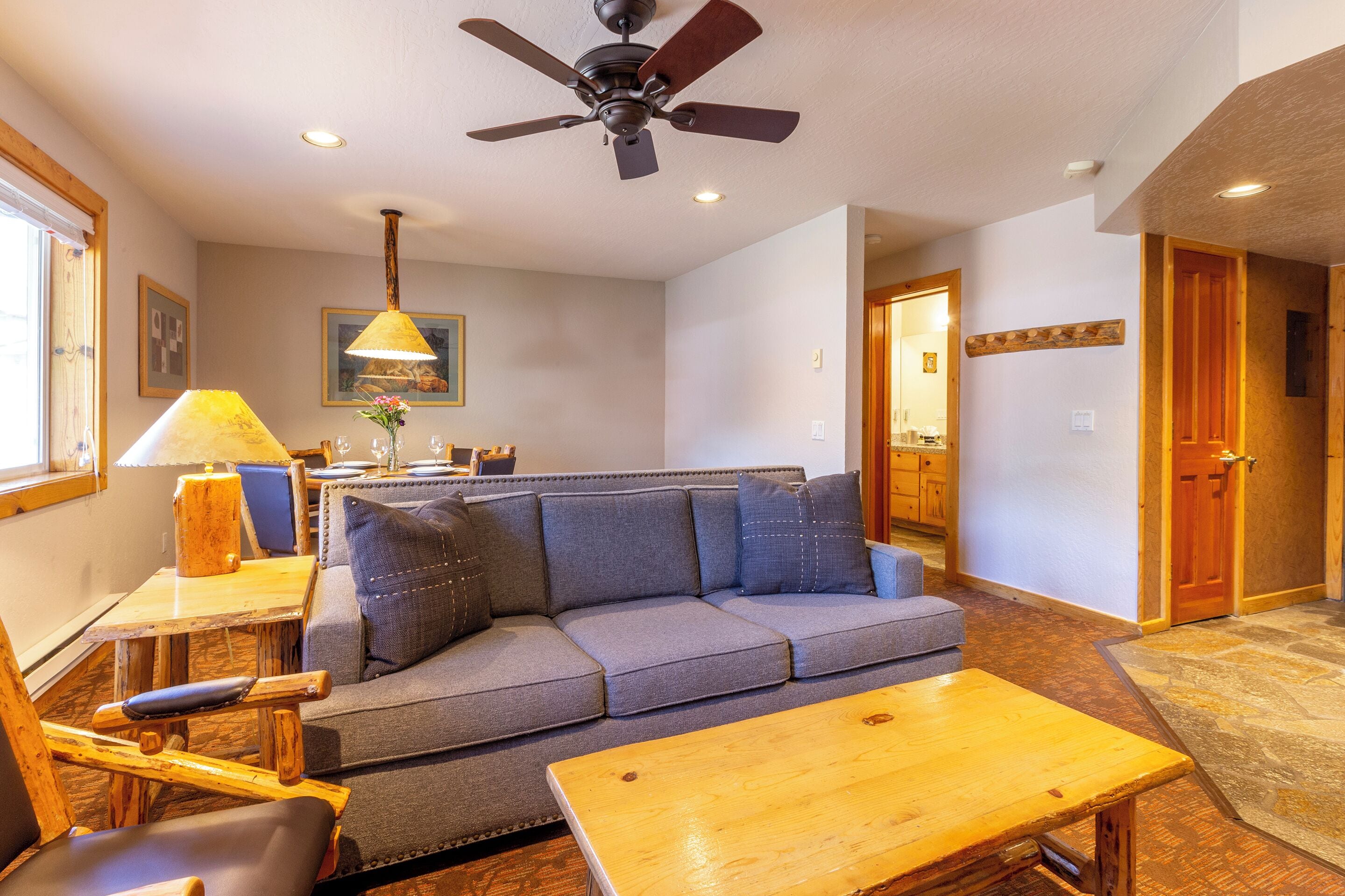 A cozy living room with a sofa, a wooden coffee table, a ceiling fan, and a dining area with a lamp.