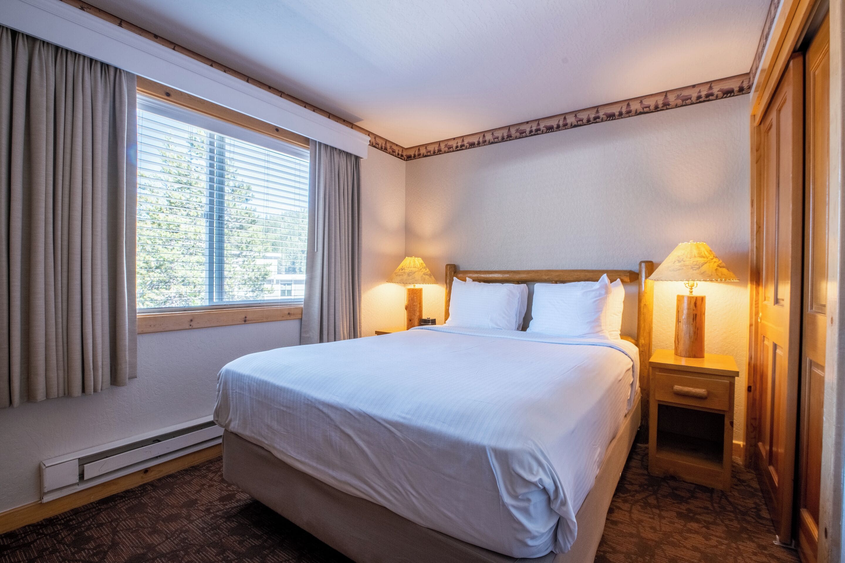 Une chambre d’hôtel avec un grand lit, deux lampes de chevet, une table de nuit en bois et une fenêtre avec des rideaux.