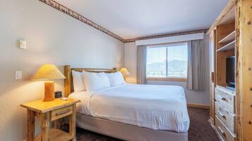 Una habitación de hotel con una cama grande, mesitas de noche de madera, un mueble para televisión y una ventana con cortinas.