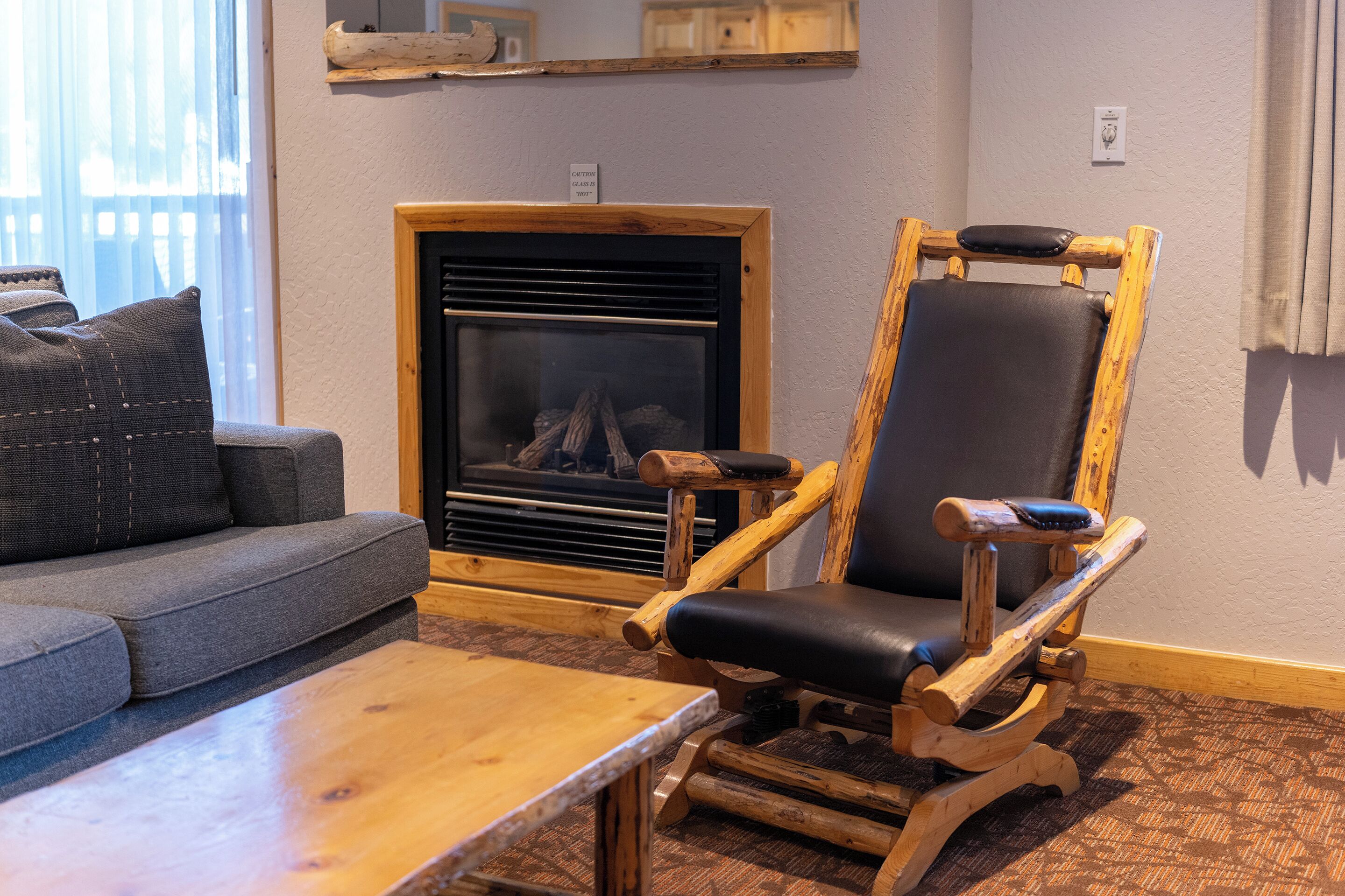 A cozy living room with a fireplace, a wooden rocking chair, and a gray sofa.