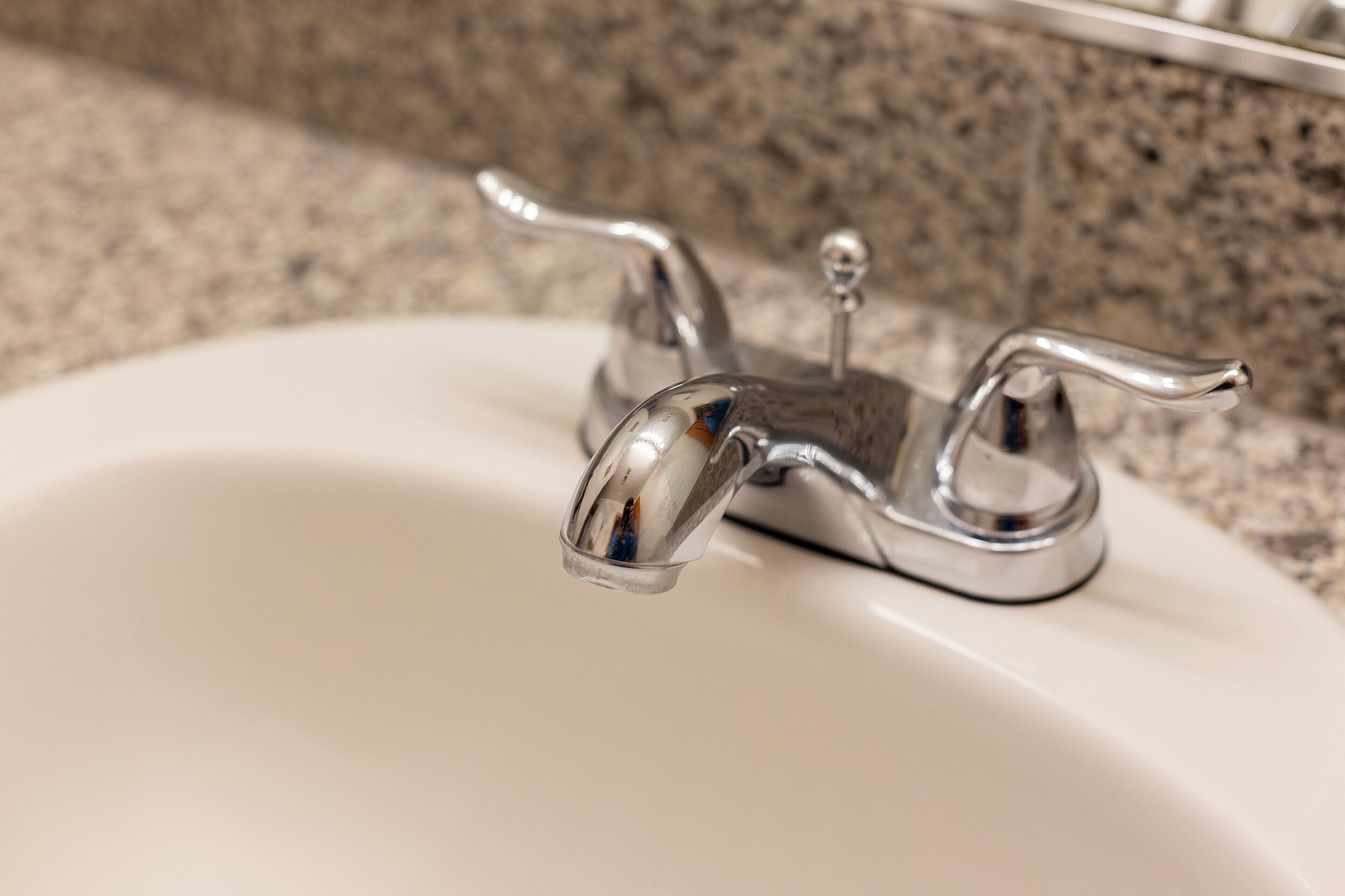 A bathroom sink with a chrome faucet and a granite countertop.