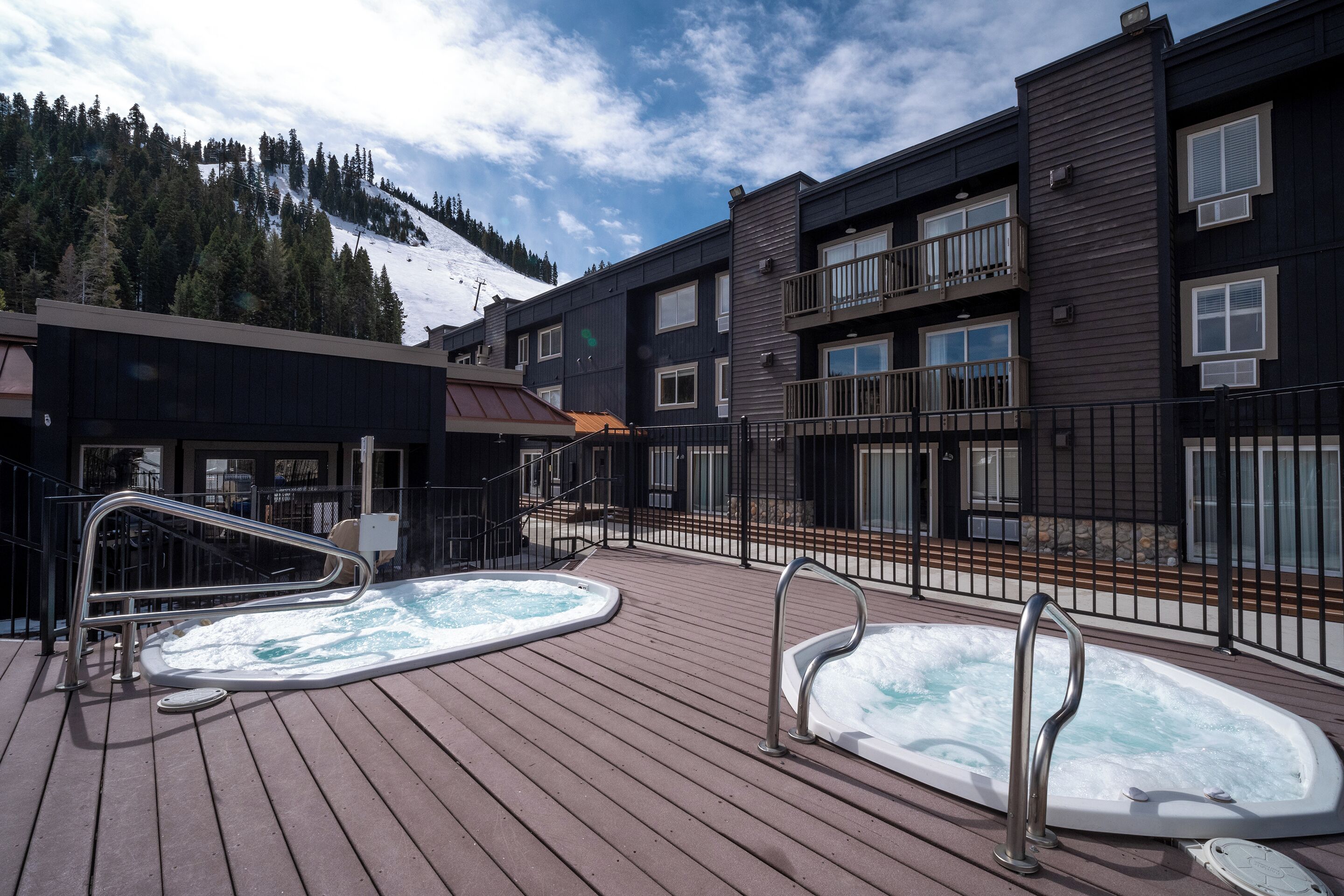 Een houten terras met twee jacuzzi's en uitzicht op de bergen.