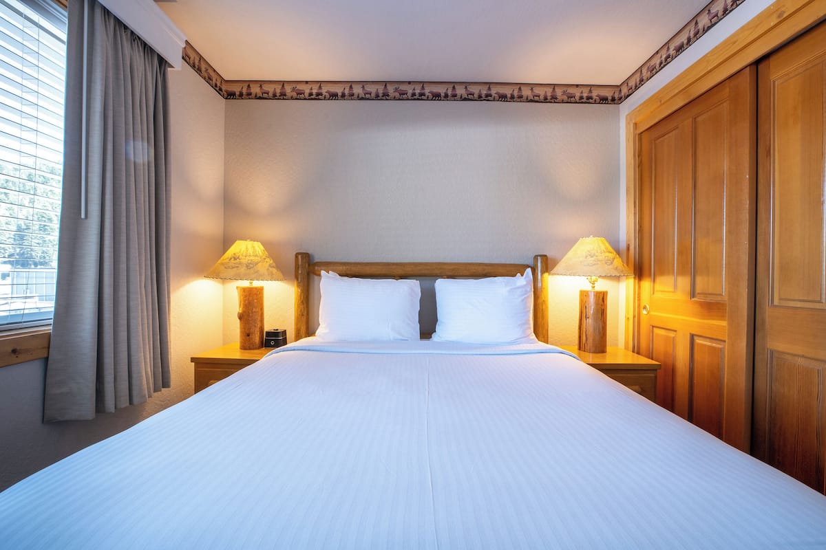 A neatly made bed with white linens, two bedside lamps, and a wooden headboard.