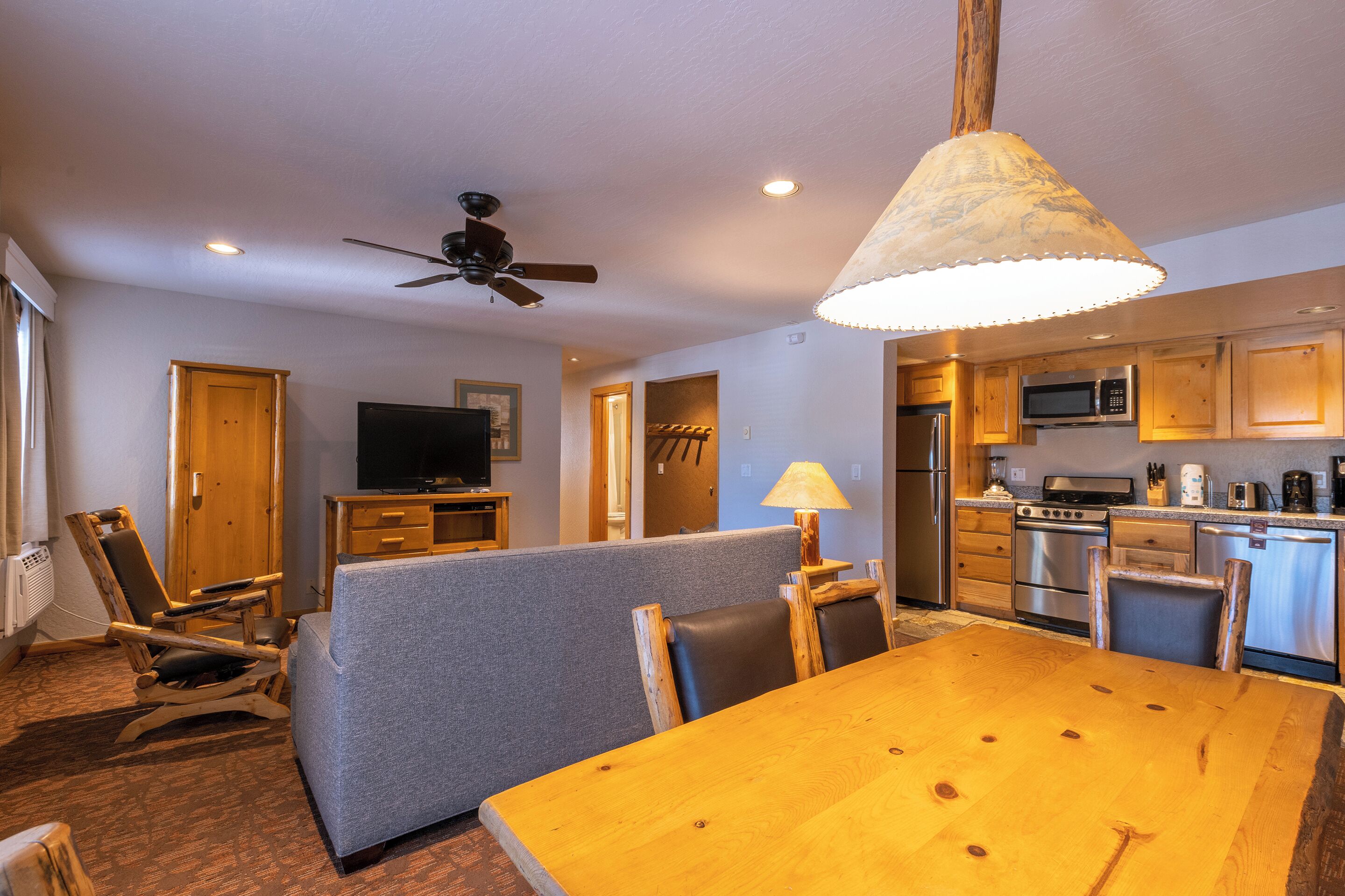 A living room with a wooden dining table, grey sofa, and a ceiling fan.